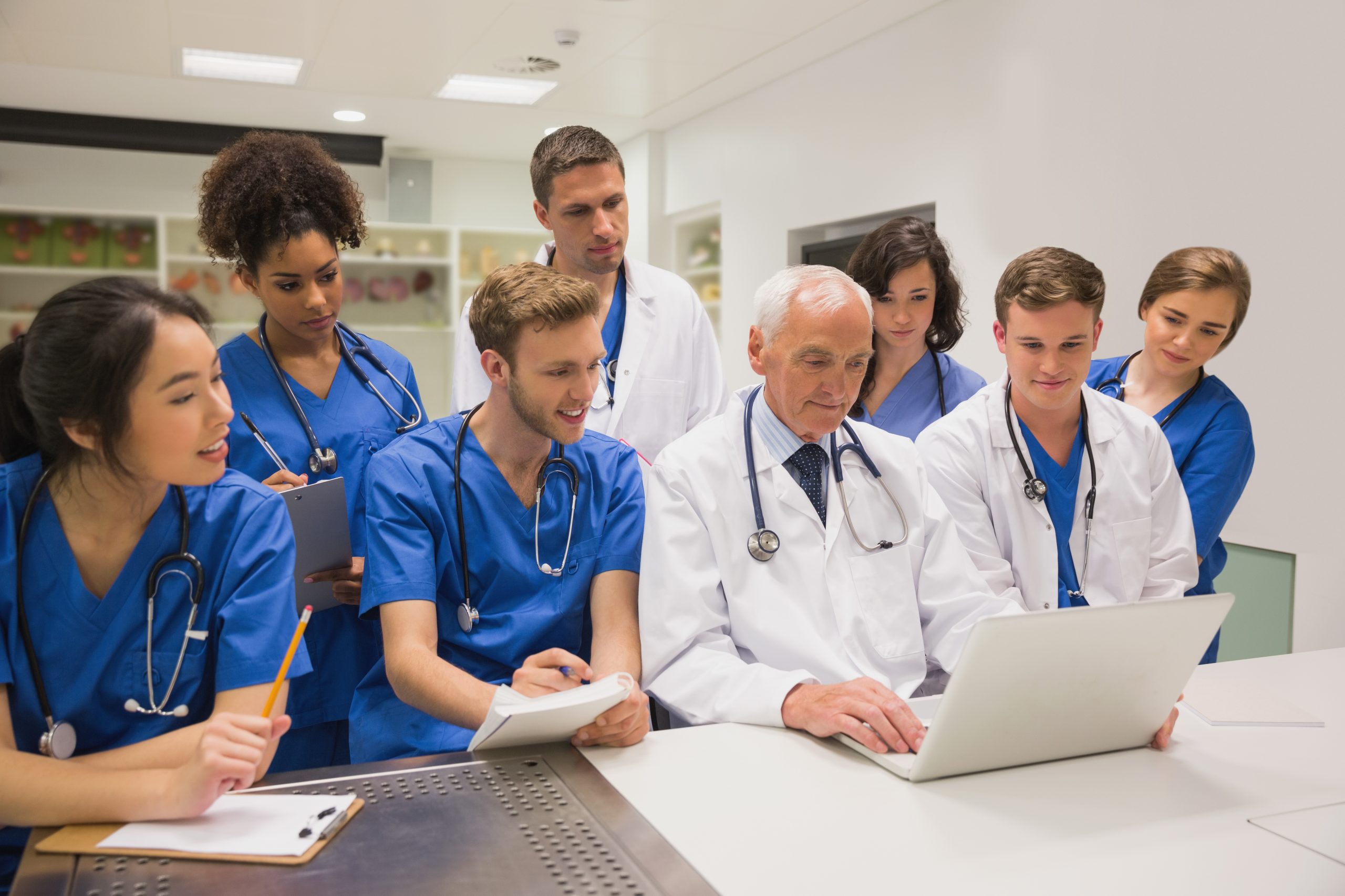 6 medical students in blue scrubs examining the doctor's charts